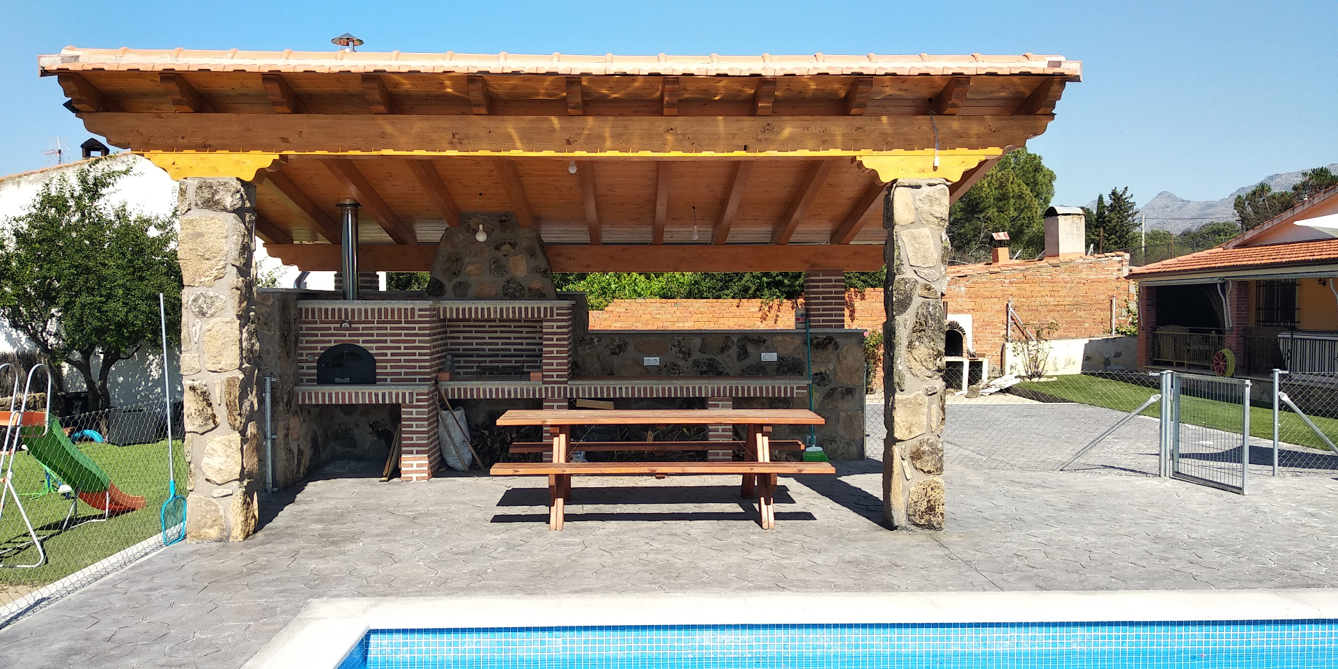Porche de piedra con barbacoa y horno junto a piscina realizado por Obras Jesús Pérez